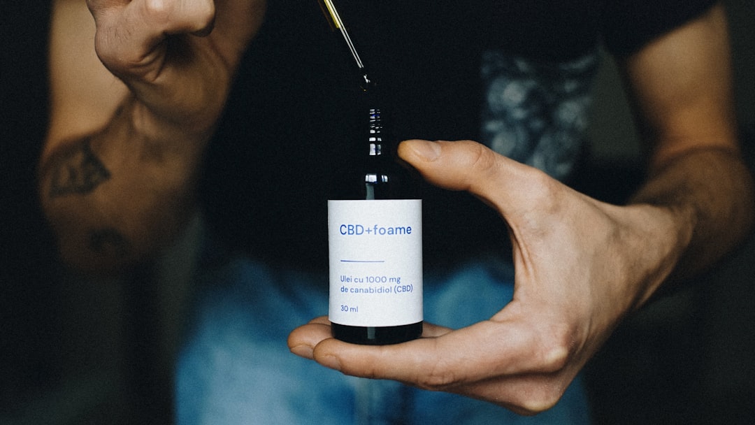 Manos aplicando aceite de masaje CBD en la piel, con un frasco de aceite y flores de cáñamo de fondo, en un ambiente de calma.
